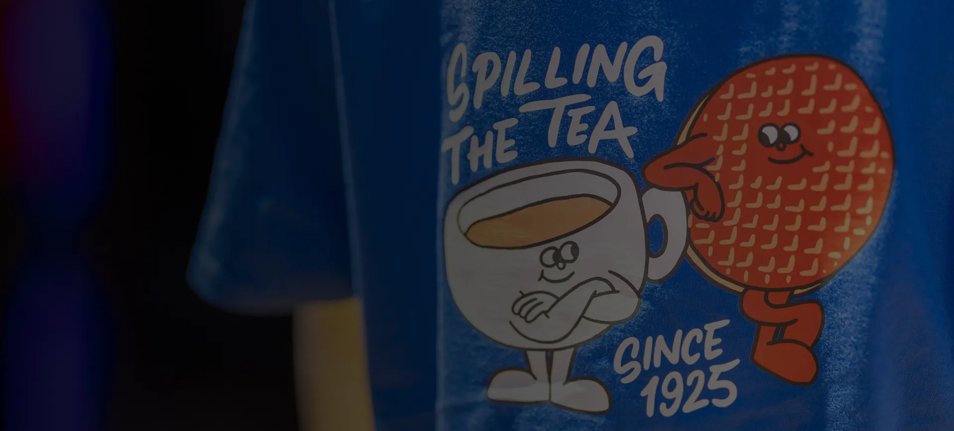 Blue McVitie's T-shirt featuring a cartoon chocolate digestive and cup of tea with the slogan “Spilling the tea since 1925.”